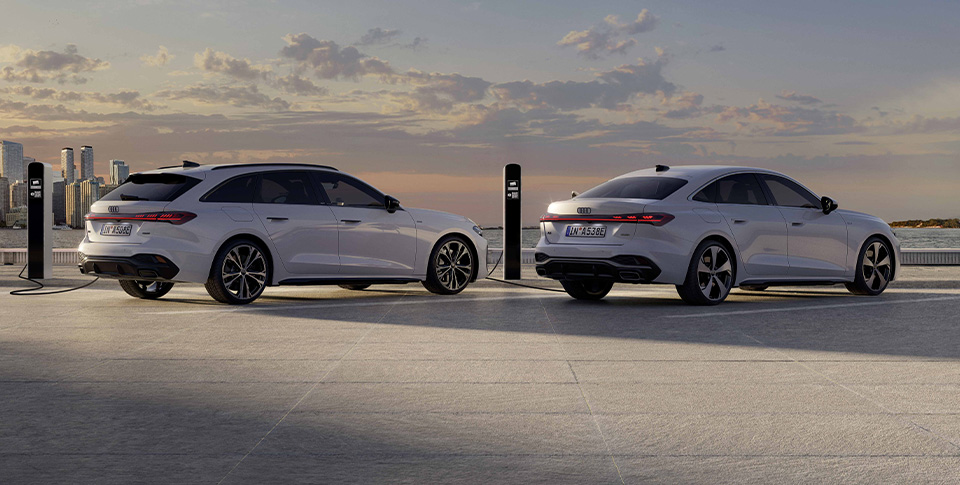 Zwei wei&szlig;e Audi Elektromodelle an E-Lades&auml;ulen mit Wolken im Hintergrund am Himmel